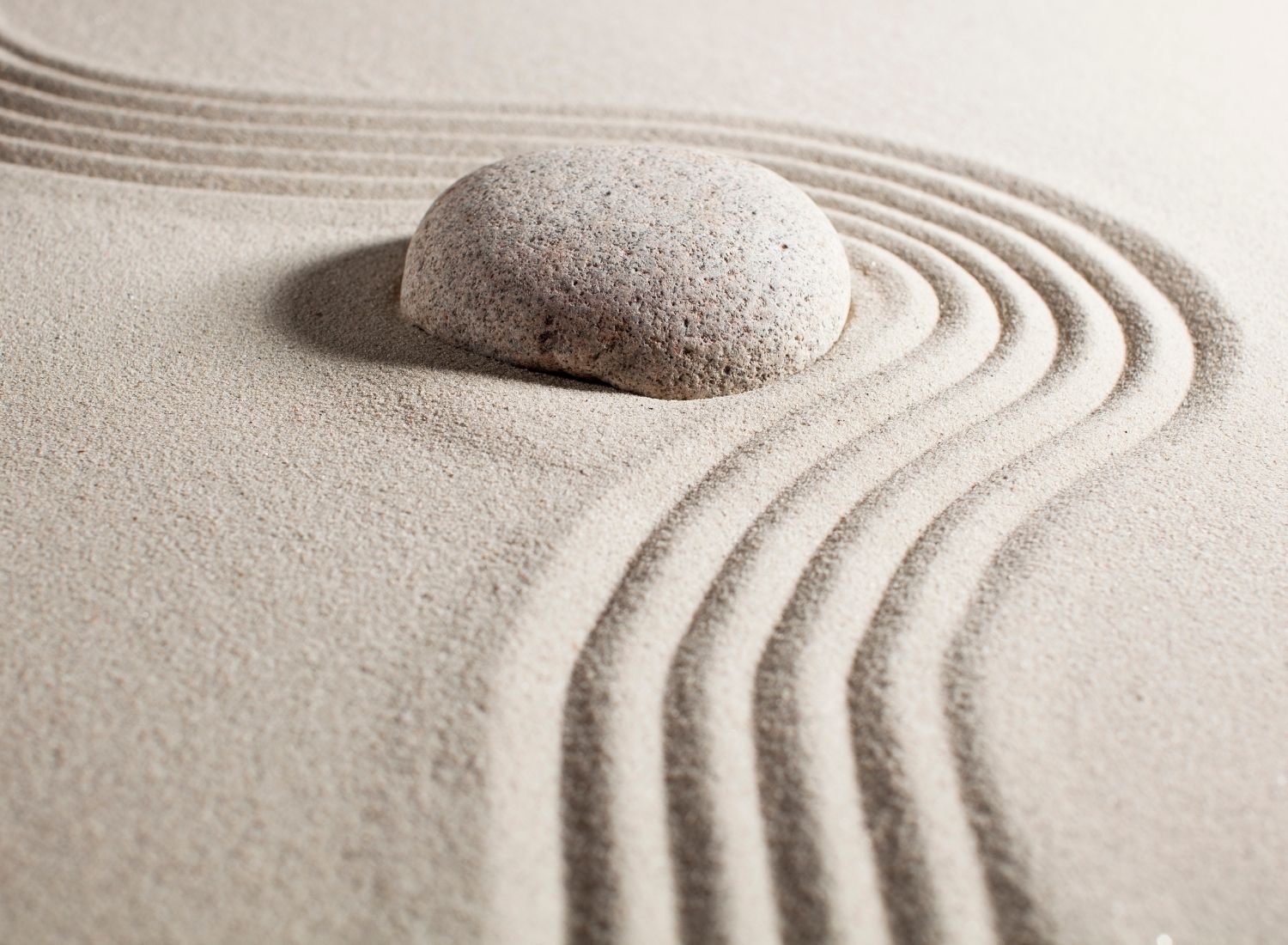 Smooth stone resting in a raked sand pattern, representing neurofunctional stability over time